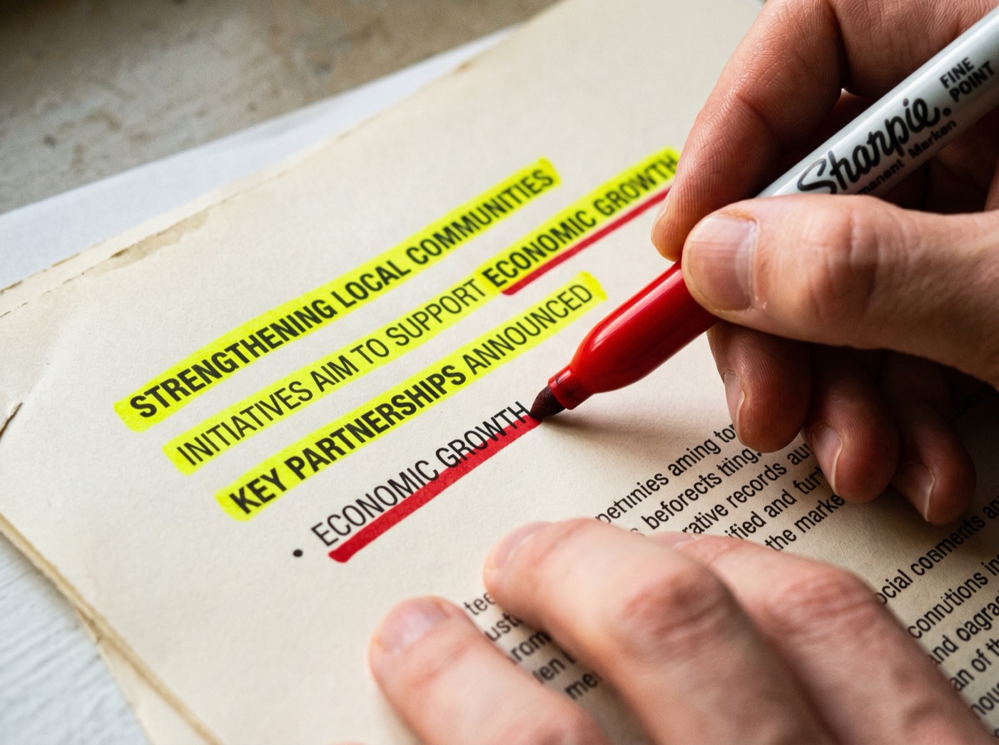 Hand holding a red Sharpie over a press release with yellow highlighter marks
