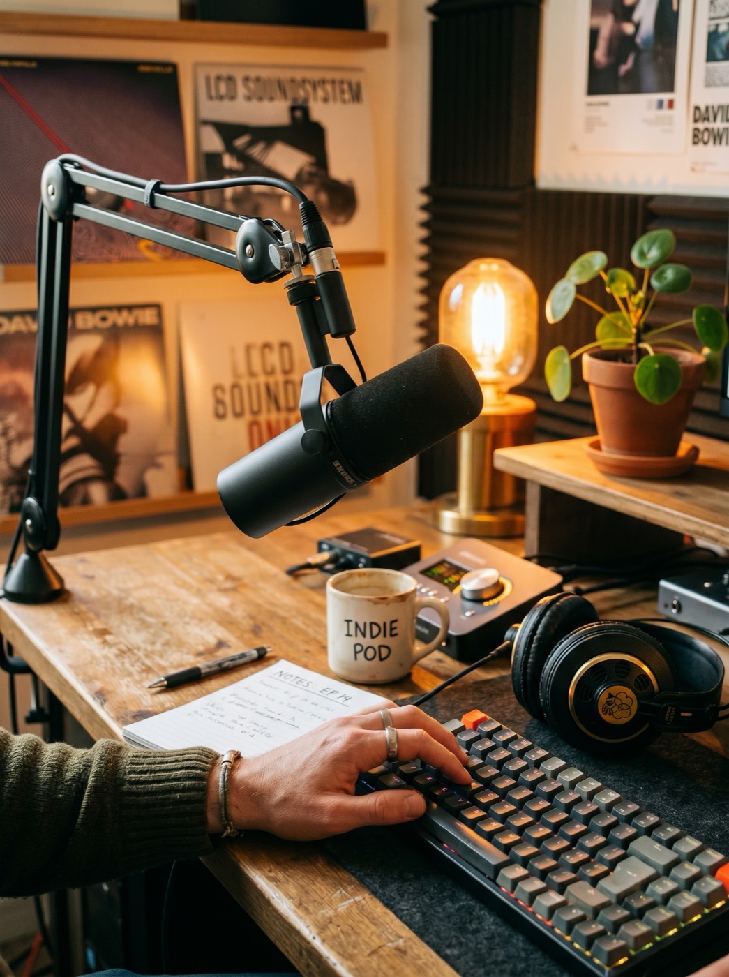 Shure SM7B microphone on a desk arm with AKG headphones and mechanical keyboard in an indie podcast studio